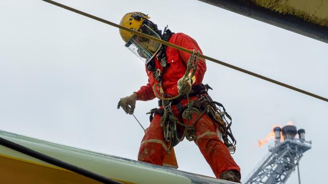 Worker wearing a full-body harness on a lifeline during fall protection training at height on an industrial platform