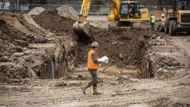Excavator digging a trench at a construction site with workers during excavation safety training