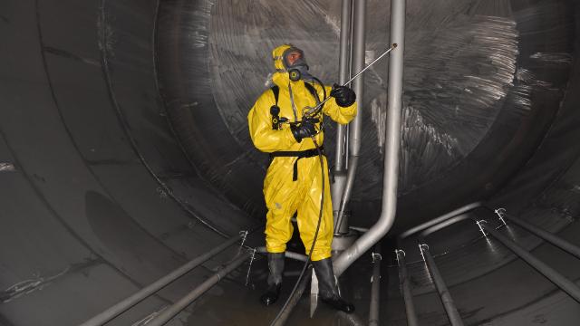 Worker in yellow protective suit inside an industrial tank during H2S safety training