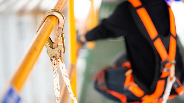 Worker in an orange harness with lanyard hooked to an anchor during construction fall protection training