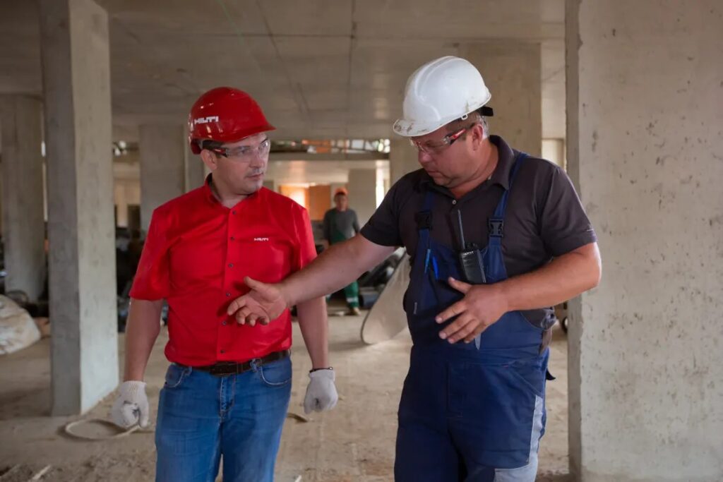 Two construction workers in hard hats discussing plans at a concrete construction site – weekly safety news update